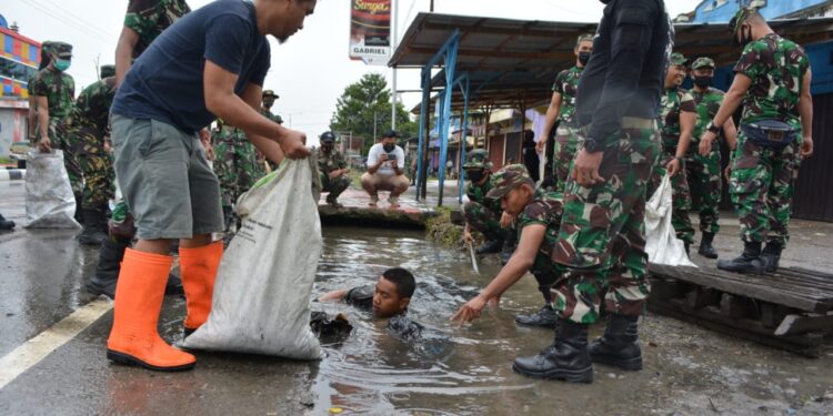 Babinsa Koramil 01 Wamena, Serda M. Ilyas  turun ke selokan air/drainase dibantu beberapa orang rekannya untuk mengeluarkan sampah yang sudah menumpuk dan menutupi drainase Jalan Trikora, Kota Wamena, Jumat (19/2/2021). Foto: Pendam Cenderawasih